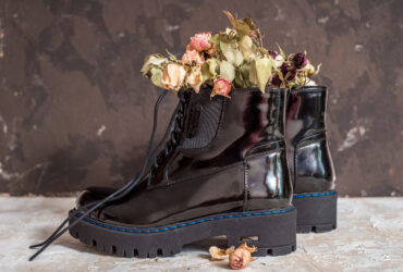 Yellow and pink flowers grow in the old black boots for original decorate. Lacquer black shoes with high soles. Gray felt bag. Concept of warm autumn or winter